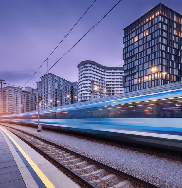 High speed train in motion on the railway station at sunset. Moving blue modern intercity passenger train, railway platform, buildings, city lights. Railroad in Vienna, Austria. Railway transportation